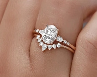 May include: A rose gold engagement ring set with an oval-shaped center stone and a delicate band with smaller stones. The ring is on a finger.