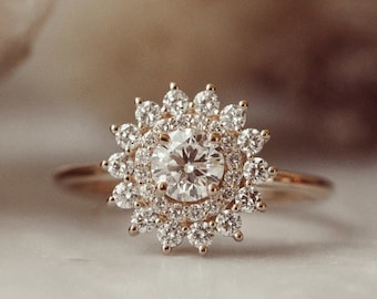 May include: A gold ring with a large, round, clear diamond surrounded by smaller diamonds in a flower-like design.