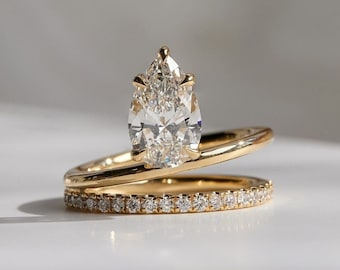 May include: A pear-shaped diamond engagement ring set in a gold band with a matching diamond band. The ring is set on a white surface.