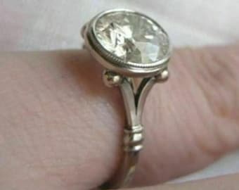 May include: A silver ring with a large, round, clear gemstone set in a bezel setting. The ring has a delicate, ornate design with small, round accents on the band.
