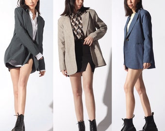 Può includere: Tre donne indossano blazer di colori diversi. La donna a sinistra indossa un blazer grigio scuro, la donna al centro indossa un blazer marrone chiaro e la donna a destra indossa un blazer blu chiaro. Tutte e tre le donne indossano stivali neri.