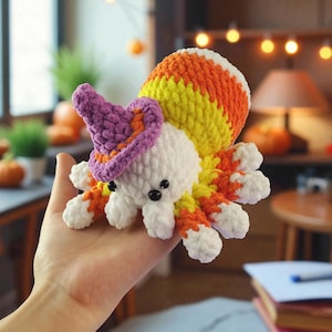 May include: A handmade crochet octopus in white, orange, yellow, and purple. The octopus is wearing a purple witch hat with orange trim. The octopus has black button eyes. The octopus is held in a hand.