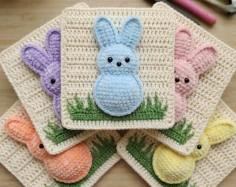 Könnte beinhalten: Eine Sammlung von fünf gehäkelten Osterhasenquadraten in Pastellfarben: Blau, Lila, Rosa, Orange und Gelb. Jeder Hase ist an einem cremefarbenen Quadrat mit grünen Grasdetails befestigt. Häkelnadeln und Scheren befinden sich im Hintergrund.