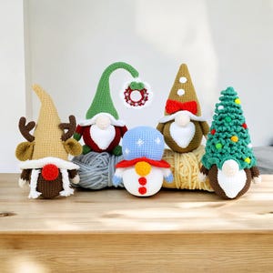 May include: Five crocheted Christmas ornaments, including a snowman, a reindeer, a gnome wearing a red hat, a gnome wearing a brown hat, and a gnome wearing a green hat with a wreath.