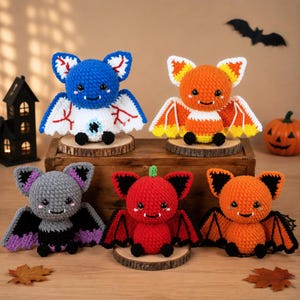 Può includere: Cinque pipistrelli all'uncinetto in vari colori e motivi. La fila superiore presenta un pipistrello blu con venature rosse e uno bianco con i colori del candy corn. La fila inferiore include un pipistrello grigio, uno rosso e uno arancione.