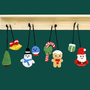 May include: A set of seven crocheted Christmas ornaments hanging from a wooden shelf. The ornaments include a snowman, a candy cane, a gingerbread person, a bell, a Christmas tree, a Santa Claus, and a blue and white ornament.
