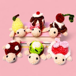 May include: Six crocheted turtle plush toys with different colored shells. The shells are decorated with a pear, a slice of kiwi, a strawberry, a cherry, a mushroom, and a scoop of ice cream with a cherry on top.