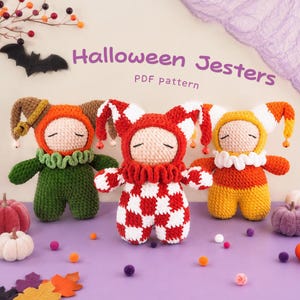May include: Three crocheted jester dolls with closed eyes and ruffled collars. The left doll is orange and green, the center doll is red and white checkered, and the right doll is yellow, orange, and white. Text reads Halloween Jesters PDF pattern.