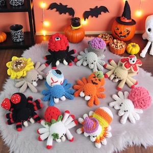May include: A collection of handmade crochet spiders in various colors and designs, including a sunflower, an eyeball, and a pumpkin. The spiders are arranged on a fluffy gray rug, with Halloween decorations in the background.