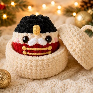 Peut inclure: Une figurine casse-noisette au crochet avec un chapeau noir, une moustache blanche et une veste rouge &agrave; bordure dor&eacute;e, nich&eacute;e dans un contenant rond au crochet couleur cr&egrave;me avec un couvercle assorti dot&eacute; d'une petite anse.