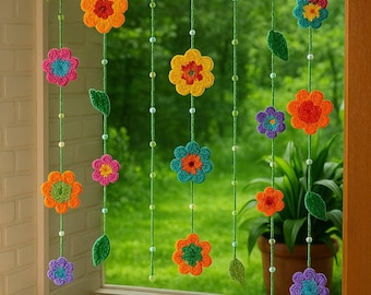 May include: A colorful crochet flower curtain with various sized flowers in shades of orange, yellow, blue, pink, and purple. The flowers are strung on green yarn with small beads and green leaf accents. A decorative watering can sits below the curtain.