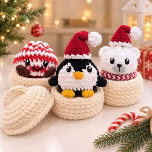 Peut inclure: Trois figurines en peluche crochetées dans des paniers en fil de couleur crème. L'une est un tourbillon de menthe poivrée rouge et blanc, une est un pingouin noir et blanc avec un bonnet de Père Noël rouge, et une est un ours polaire blanc.
