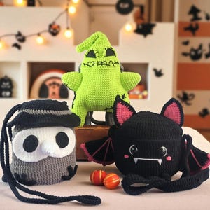 May include: A selection of handmade crochet Halloween items. Features a green Oogie Boogie plush, a black bat-shaped bag with pink details, and a grey owl-shaped bag with a black hat. Two small orange and red decorative balls are in front.