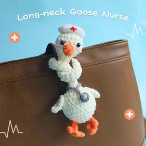 Op de afbeelding: Een gehaakt ganzen-speelgoed, verkleed als verpleegster, met een witte hoed met een rood kruis en een grijze stethoscoop. De gans heeft een oranje snavel en poten. De tekst "Long-neck Goose Nurse" staat boven de gans. Het is bevestigd aan een bruine leren tas.