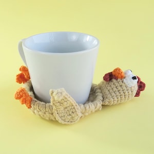 May include: A white ceramic mug rests on a handmade crochet coaster. The coaster is beige with orange and red accents, shaped like a whimsical creature. The background is a solid yellow.