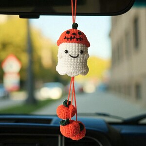 Op de afbeelding: Een handgemaakte Halloween auto-hanger met een gehaakt wit spook met een oranje pompoen hoed. Twee oranje pompoenen met groene stelen hangen eronder. De hanger is opgehangen aan een oranje touwtje.