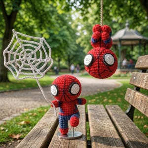 May include: Two handmade crochet figures featuring a red and blue superhero character. One figure stands on a circular metal base holding a white crocheted spider web, while the other hangs upside down from a rope, both with large white eyes.