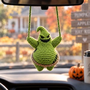 May include: A lime green crocheted figure with a pointed head, a wide jagged grin, and black stitched details, suspended by two green crocheted cords. The figure has a tan-coloured band around its midsection and is shaped like a stylised ghost.