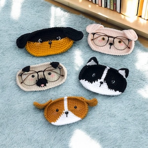 May include: Four crocheted dog-shaped eyeglass holders in different colors and patterns. The holders are made of yarn and have a cute, cartoon-like design.