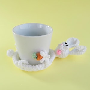 May include: A white ceramic mug with a black handle and the text "But First, Coffee" in a bold, black font. The mug is set against a blurred background, suggesting a cozy setting. The mug appears to be approximately 4 inches tall.