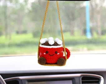 Peut inclure: Une tasse en crochet rouge avec un visage souriant et des guimauves blanches suspendues au rétroviseur d'une voiture.