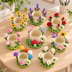 Könnte beinhalten: Eine Sammlung von acht cremefarbenen Keramiktassen, jede mit einer einzigartigen Häkelbasis und dekorativen Aufsätzen. Die Designs umfassen Sonnenblumen, Lavendel, rote Rosen, rosa Tulpen, Schmetterlinge, Pilze, Wildblumen und Calla-Lilien.