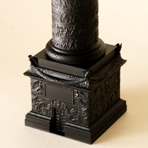 Könnte beinhalten: Eine schwarze dekorative Säule mit aufwendigen Reliefschnitzereien. Die Säule steht auf einem quadratischen Sockel, ebenfalls mit detaillierten Schnitzereien. Das Design zeigt klassische architektonische Elemente und Figuren.
