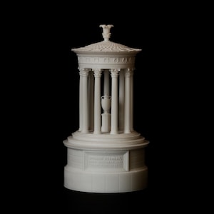 Può includere: Un modello architettonico bianco di un tempio circolare con tetto a cupola, un colonnato di colonne scanalate e un'urna centrale su un piedistallo. La base include l'iscrizione DONALD STEWART, FROM SEPTEMBER 1888 UNTIL JUNE 1889.