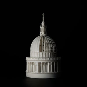 Op de afbeelding: Een gedetailleerd wit architectonisch model van een gebouw met een koepel, mogelijk een kathedraal, tegen een zwarte achtergrond. Het model toont ingewikkelde details, waaronder zuilen, bogen en een kruis op de top.