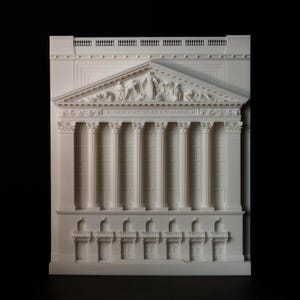 May include: A white architectural model of the New York Stock Exchange. The model features detailed columns, a triangular pediment with sculpted figures, and the text "NEW YORK STOCK EXCHANGE" across the top.