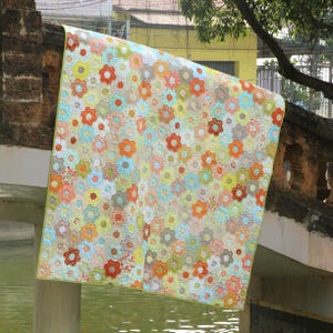 Pode incluir: Um edredom feito à mão com um padrão floral em tons de laranja, vermelho, amarelo, azul e verde. O edredom é exibido ao ar livre, drapeado sobre uma estrutura de pedra, mostrando seu design intrincado e artesanato. As bordas do edredom têm uma borda verde.