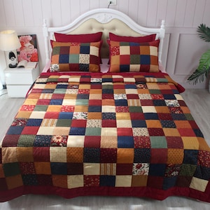 May include: A patchwork quilt and two matching pillow shams featuring a grid of squares in various colours including deep red, navy blue, mustard yellow, forest green, and cream, with some squares displaying small floral and geometric patterns.
