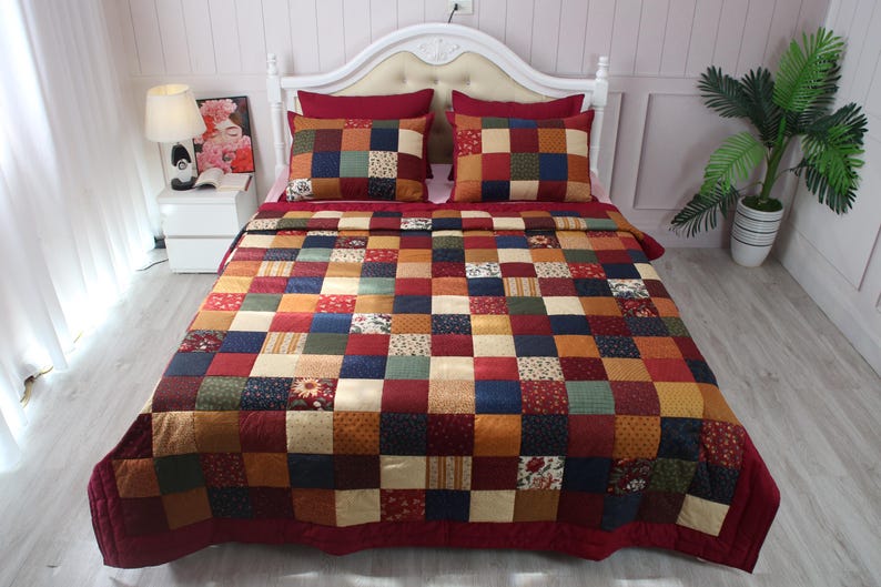 May include: A patchwork quilt and two matching pillow shams featuring a grid of squares in various colors including deep red, navy blue, mustard yellow, forest green, and cream, with some squares displaying small floral and geometric patterns.