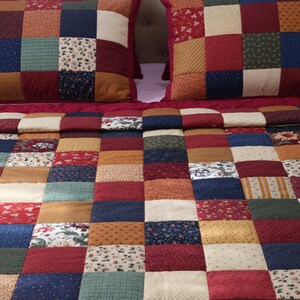 May include: A patchwork quilt and two matching pillow shams featuring a grid of square fabric patches in various colors including deep red, navy blue, forest green, mustard yellow, and cream, with assorted floral and geometric patterns.