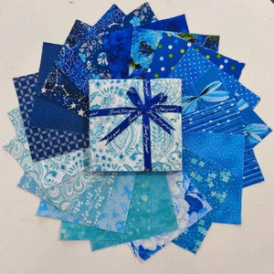 May include: A circular arrangement of blue fabric squares, with a gift box at the centre. The box is wrapped in patterned paper and tied with a blue ribbon, which reads "Just for you". The fabrics display various shades of blue and diverse patterns.