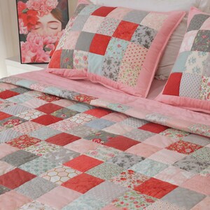Puede incluir: Una colcha de patchwork rosa con una variedad de patrones florales y geom&eacute;tricos en tonos de rosa, rojo, gris y azul. La colcha est&aacute; hecha de cuadrados y est&aacute; doblada sobre una cama con dos almohadas de patchwork a juego.