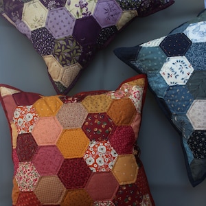 Könnte beinhalten: Drei Patchwork-Kissen mit sechseckigen Mustern. Die Kissen sind aus verschiedenen Stoffen mit floralen und geometrischen Mustern gefertigt. Die Kissen sind in den Farben Lila, Blau, Rot, Orange und Gelb gehalten.