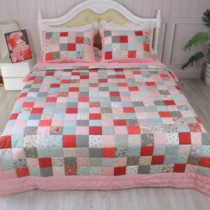 Puede incluir: Un edred&oacute;n de patchwork con un borde rosa y una variedad de patrones florales y geom&eacute;tricos en tonos de rojo, rosa, gris y verde. El edred&oacute;n est&aacute; sobre una cama blanca con dos fundas de almohada a juego.