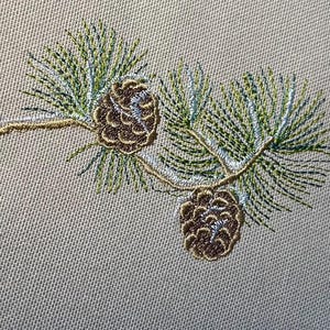Może przedstawiać: Haftowany wzór dwóch szyszek na gałęzi z zielonymi i srebrnymi igłami.