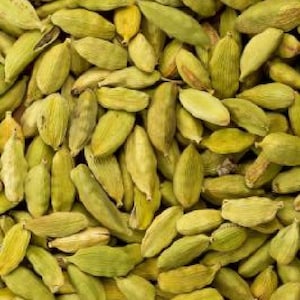 Könnte beinhalten: Ein Nahaufnahmebild eines Stapels grüner Kardamomkapseln. Die Kapseln sind in einem zufälligen Muster angeordnet, wobei sich einige Kapseln überlappen. Die Kapseln sind alle etwa gleich groß und geformt und haben eine leicht runzelige Textur.