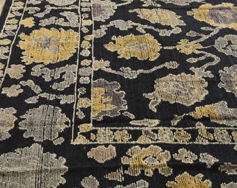 Puede incluir: Una alfombra negra y crema con un diseño floral. La alfombra tiene un borde de flecos.