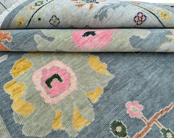 May include: Close-up of a rolled-up rug with a floral pattern. The rug has a light blue background with pink, yellow, and green floral designs. The edges of the rug are visible, showing a fringe detail.