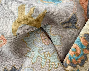 May include: A close-up of a light gray rug with a colorful abstract pattern. The rug has a soft, textured surface and features shades of blue, pink, orange, and yellow.