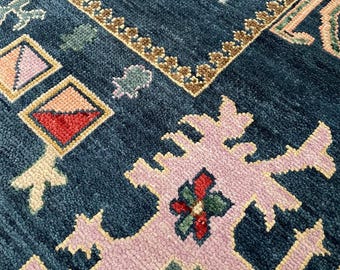 Könnte beinhalten: Nahaufnahme eines blauen Teppichs mit aufwendigen Mustern. Der Teppich zeigt geometrische Formen und florale Designs in Rosa, Grün und Braun. Die Handwerkskunst zeigt sich in der Textur und den Farbvariationen.