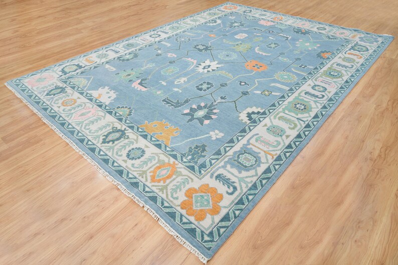 K&ouml;nnte beinhalten: Ein blauer Teppich mit einem wei&szlig;en und gr&uuml;nen Rand. Der Teppich hat ein Blumenmuster mit orangefarbenen, rosa und gr&uuml;nen Akzenten.