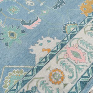 K&ouml;nnte beinhalten: Ein blauer Teppich mit einem wei&szlig;en und t&uuml;rkisfarbenen Rand. Der Teppich hat ein geometrisches Muster mit rosa, gr&uuml;nen und gelben Akzenten.