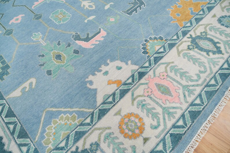 K&ouml;nnte beinhalten: Ein blauer Teppich mit einem wei&szlig;en und t&uuml;rkisfarbenen Rand. Der Teppich hat ein geometrisches Muster mit rosa, gr&uuml;nen und gelben Akzenten.