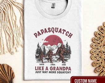 May include: White t-shirt with a graphic of three Bigfoot figures walking in a forest with a red sun in the background. The text "Papasquatch" is above the figures and the text "Like a Grandpa Just Way More Squatchy" is below the figures. The names "David", "Linda", and "John" are written below the figures. The text "Custom Name (Up to 6 Kids)" is at the bottom of the shirt.