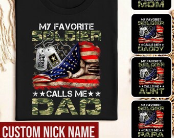 May include: Black t-shirt with a camouflage and American flag design. The text "My Favorite Soldier Calls Me Dad" is printed on the shirt. The text "Custom Nick Name" is printed below the design.