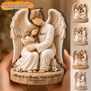 Pode incluir: Uma estatueta de anjo bege retratando um pai e sua filha em um abraço carinhoso. A base está inscrita com "Always in our Thoughts - Forever in our Hearts" e um nome e datas. O texto "APPEARANCE AND NAME CAN BE CHANGED" também é visível.